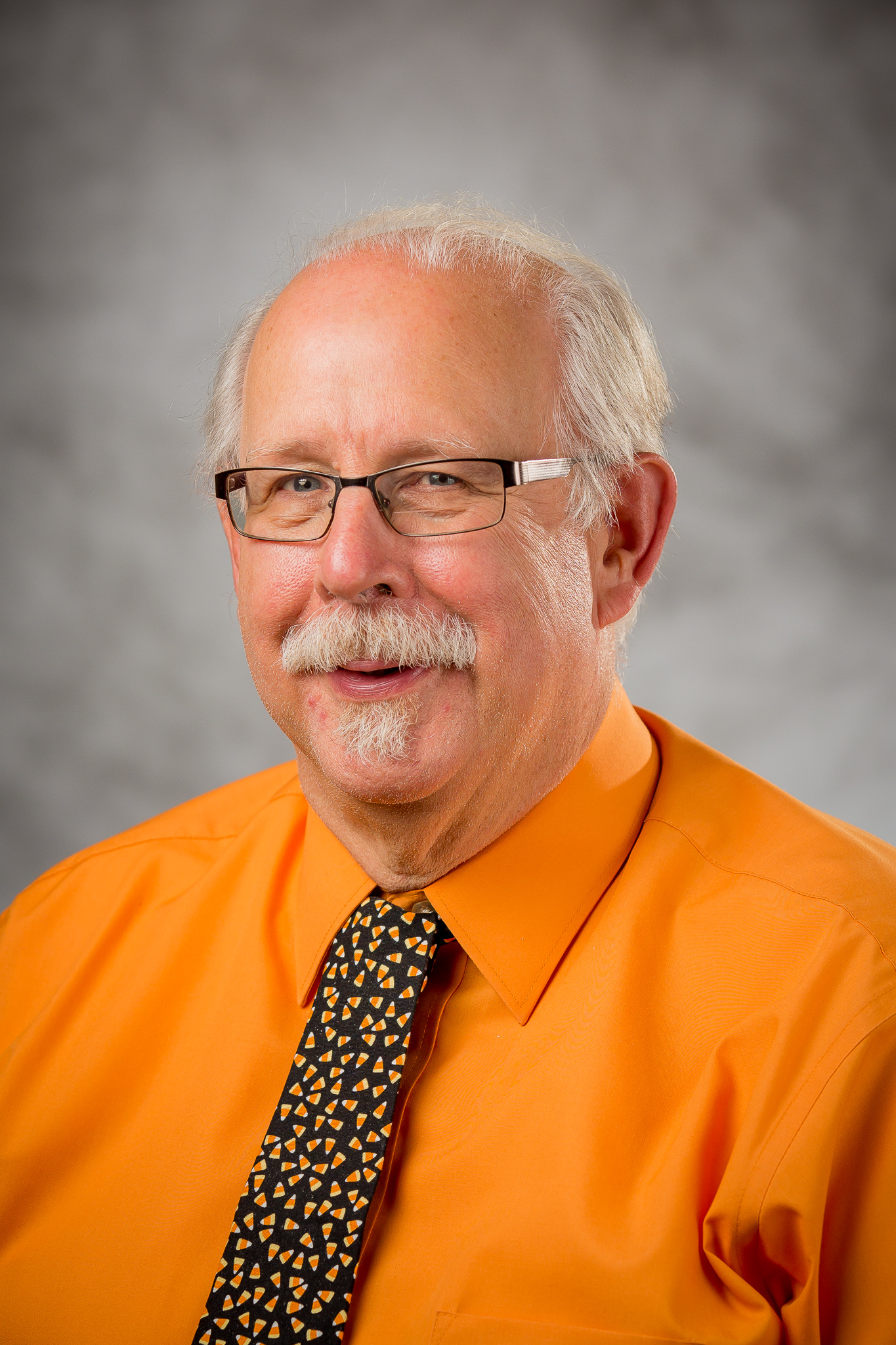 picture of a man with glasses and a orange button up shirt with a candy-corn tie